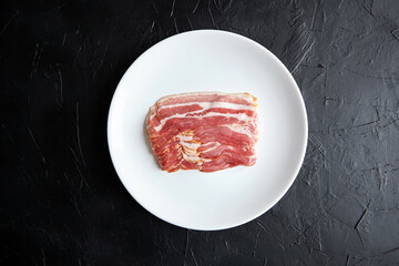 Bacon strips, raw smoked pork meat slices on white plate on black table