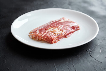 Bacon strips, raw smoked pork meat slices on white plate on black table