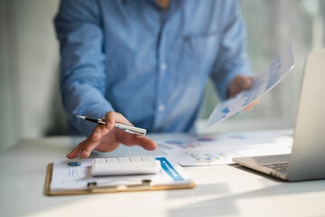 Businessman using calculator and laptop for doing math finance on wooden desk in office and business working background, tax, accounting, statistics, and analytic research concept