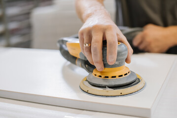 An employee of a furniture factory sands a wooden surface with a sander - 498494280