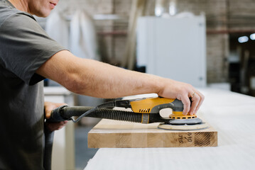 An employee of a furniture factory sands a wooden surface with a sander - 498494290