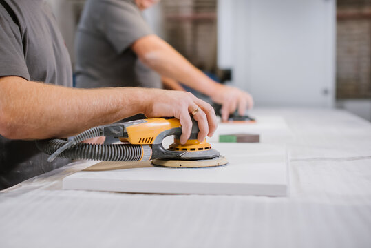 An employee of a furniture factory sands a wooden surface with a sander