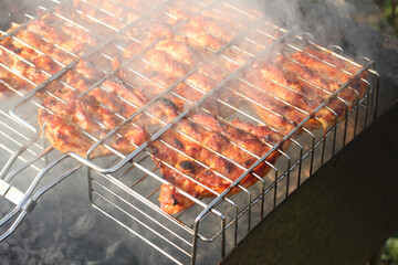 Pieces of chicken, squeezed between grill grates, frying on a grill brazier. Closeup