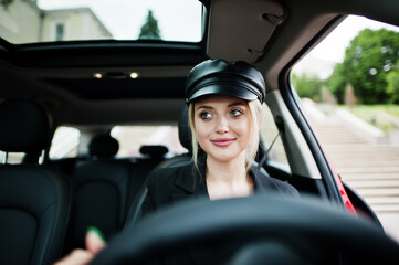 Portrait of beautiful blonde sexy fashion woman model in cap and in all black with bright makeup sit and drive red city car.