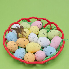 Basket with eggs in different colors and a dinosaur on them on a green background. Minimal Easter scene.