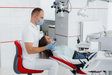 Fototapeta premium A young dentist specialist examines and treats the teeth of a beautiful woman in modern white dentistry. Dental prosthetics, treatment and teeth whitening. Modern dentistry.