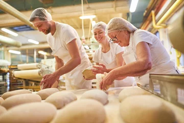 Gordijnen Senior vrouw als bakker met een team dat een brood bakt © Robert Kneschke