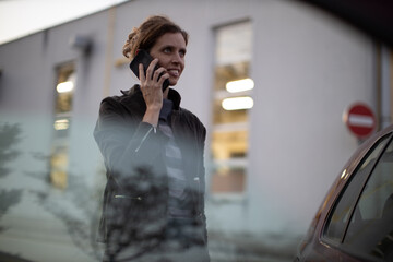 Woman talking on a phone on a street close to her car