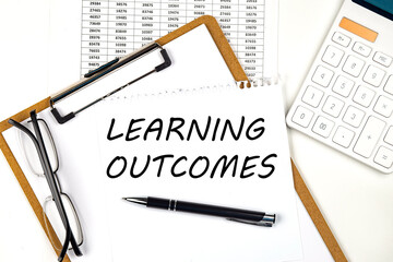 Text LEARNING OUTCOMES on the white paper on clipboard with chart and calculator
