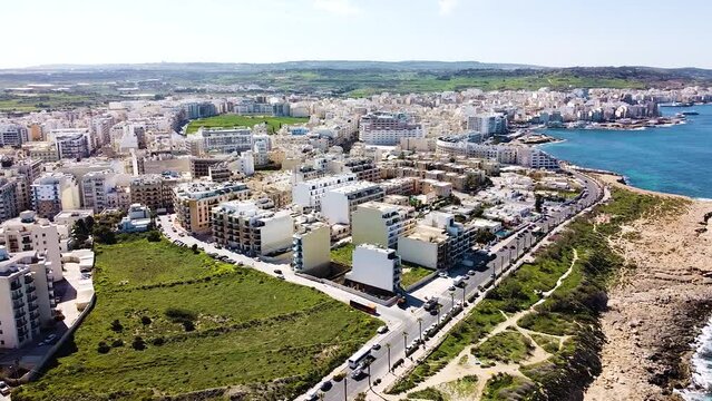 Malta's town situated on rocky coastline with beautiful buildings and green meadows, aerial view
