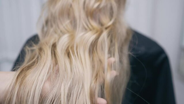The hairdresser makes a hairstyle for a girl with long blond hair in the salon