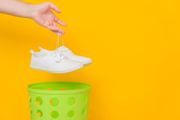Shoes are thrown into the trash, yellow background, side view, space for text.