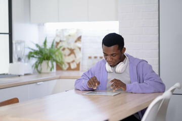 Black man using digital tablet on kitchen at home, working office work remotely typing text, African american freelancer using notepad computer Distance learning online education and work.