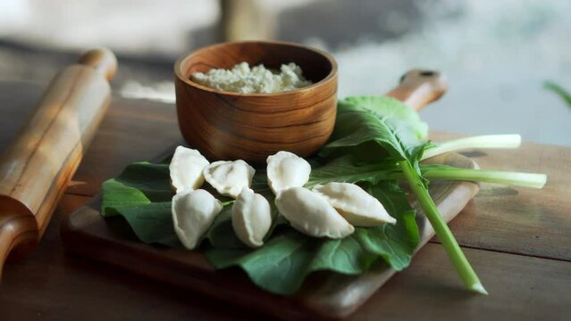 Traditional Russian fresh handmade dumplings lying on a wooden table on a cutting board with cottage cheese in a wooden plate and spinach