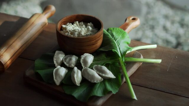 Traditional Russian fresh handmade dumplings lying on a wooden table on a cutting board with cottage cheese in a wooden plate and spinach