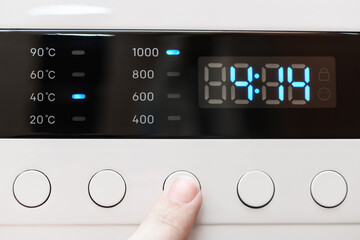 Washing machine display close up ,time remaining four hour 14 minutes during washing process. Finger selects wash mode. Abstract laundry programming backdrop