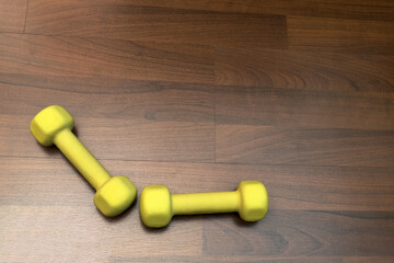 Yellow dumbbells at an obtuse angle frame the background of brown boards, fitness and healthy lifestyle