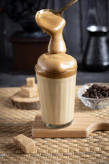 Iced Dalgona Coffee, a trendy fluffy creamy whipped coffee, on a dark wooden background with coffee...