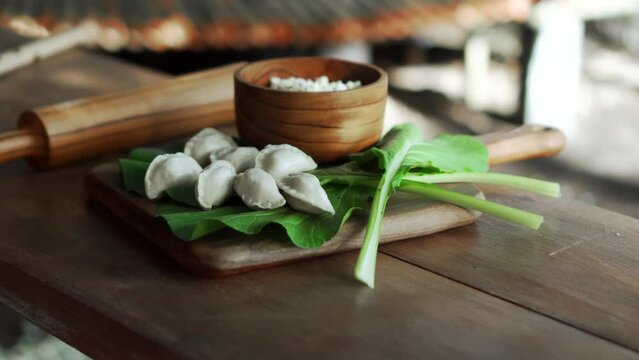 Traditional Russian fresh handmade dumplings lying on a wooden table on a cutting board with cottage cheese in a wooden plate and spinach