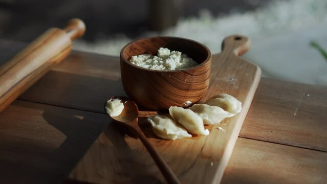 Russian fresh handmade dumplings lying on a wooden table on a cutting board with cottage cheese in a wooden plate