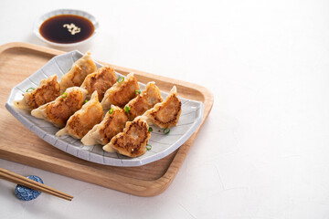 Pan-fried gyoza dumpling jiaozi in a plate with soy sauce on white table background.