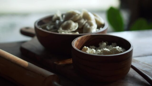 Russian fresh handmade dumplings lying on a wooden table on a cutting board with cottage cheese in a wooden plate