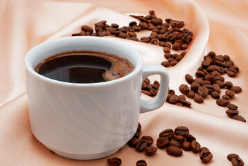cup of black coffee on pink satin with roasted coffee beans