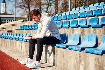Man in sportswear sitting on stadium seat and browsing smartphone, Male sportsman check fitness...