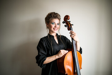 portrait of a cellist girl against a light gray wall, a woman with a cello smiles © Ринат Куйшин