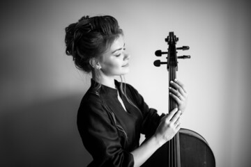 black and white portrait of a cello girl against a light gray wall, a woman holding a cello neck in...