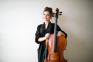 portrait of a cellist girl on a light background, a woman stands with a cello on a white light...