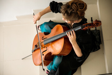 cellist sits on the stairs and plays the cello, top view © Ринат Куйшин
