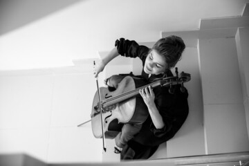 cellist sits on the stairs and plays the cello, enjoys playing music, top view, black and white...