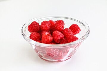 A glass bowl of juicy raspberries on a clean white table