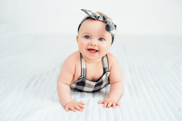 Seven month old baby child sitting on bed. Cute smiling little infant girl on white soft blanket. girl wearing headband. Charming blue-eyed baby. Copy space.