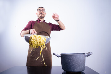 Caucasian white man with apron and funny face cooking spaghetti at home, tossing the pasta in a pan by dropping it on a white background in horizontal shot