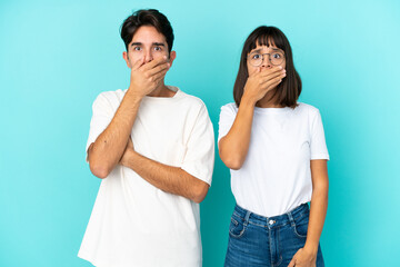 Young mixed race couple isolated on blue background covering mouth with hands for saying something inappropriate