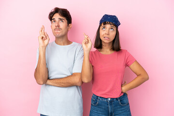 Young couple isolated on pink background with fingers crossing and wishing the best
