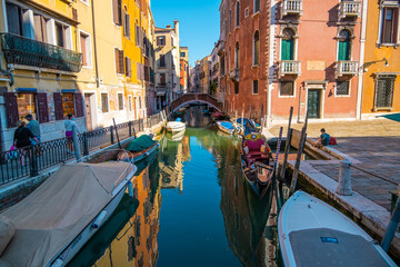 View of empty gondola on narrow canals, with a tourist waiting for the gondolier of Venice, Italy.