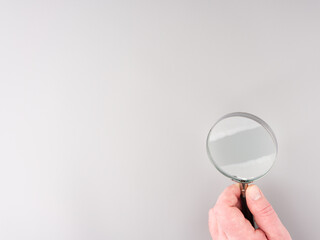 Magnifying glass in a hand on a gray background. Space for text