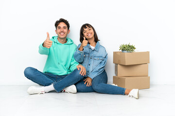 Young couple making a move while picking up a box full of things sitting on the floor isolated on white background giving a thumbs up gesture because something good has happened