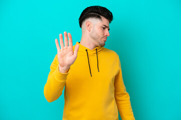 Young caucasian man isolated on blue background making stop gesture and disappointed