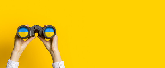 female hands hold black binoculars on a bright yellow background - Powered by Adobe