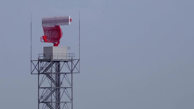 A crow flying in front of a radar dish at an airfield