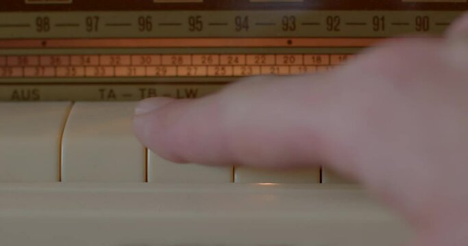 Close-up of a finger presses the button of an old radio. It selects the waveband to listen to. Frequency selection.