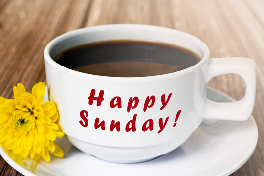 Happy sunday text on white coffee cup with yellow flower on wooden desk.