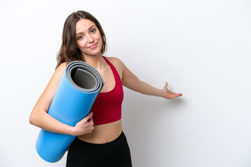 Young sport caucasian woman going to yoga classes while holding a mat isolated on white background extending hands to the side for inviting to come