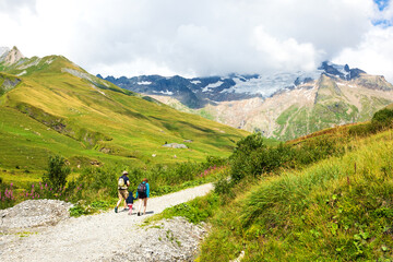 Family with little child (unrecognizable; back view) hiking in French Alps in summer. The Aiguille des Glaciers, mountain in the Mont Blanc massif. View From Chapieux valley, Savoie, France.
