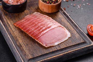 Smoked ham on a dark concrete table with addition of fresh aromatic herbs and spices