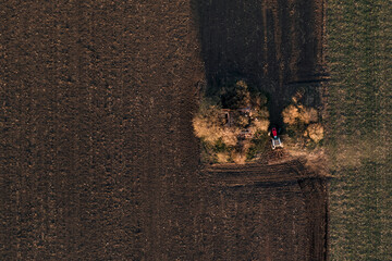 Agricultural tractor with tiller attached performing soil tillage in field, aerial view